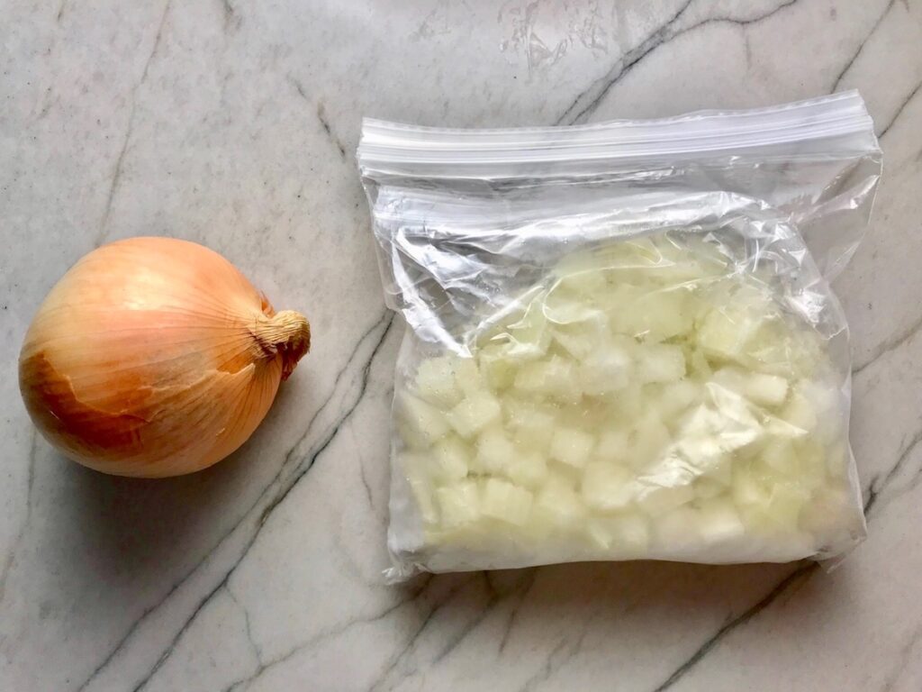 Whole onion with skin on the left and diced frozen onion in a baggie to the right for the post 'Can you freeze pulled pork - Freezer Tips.'