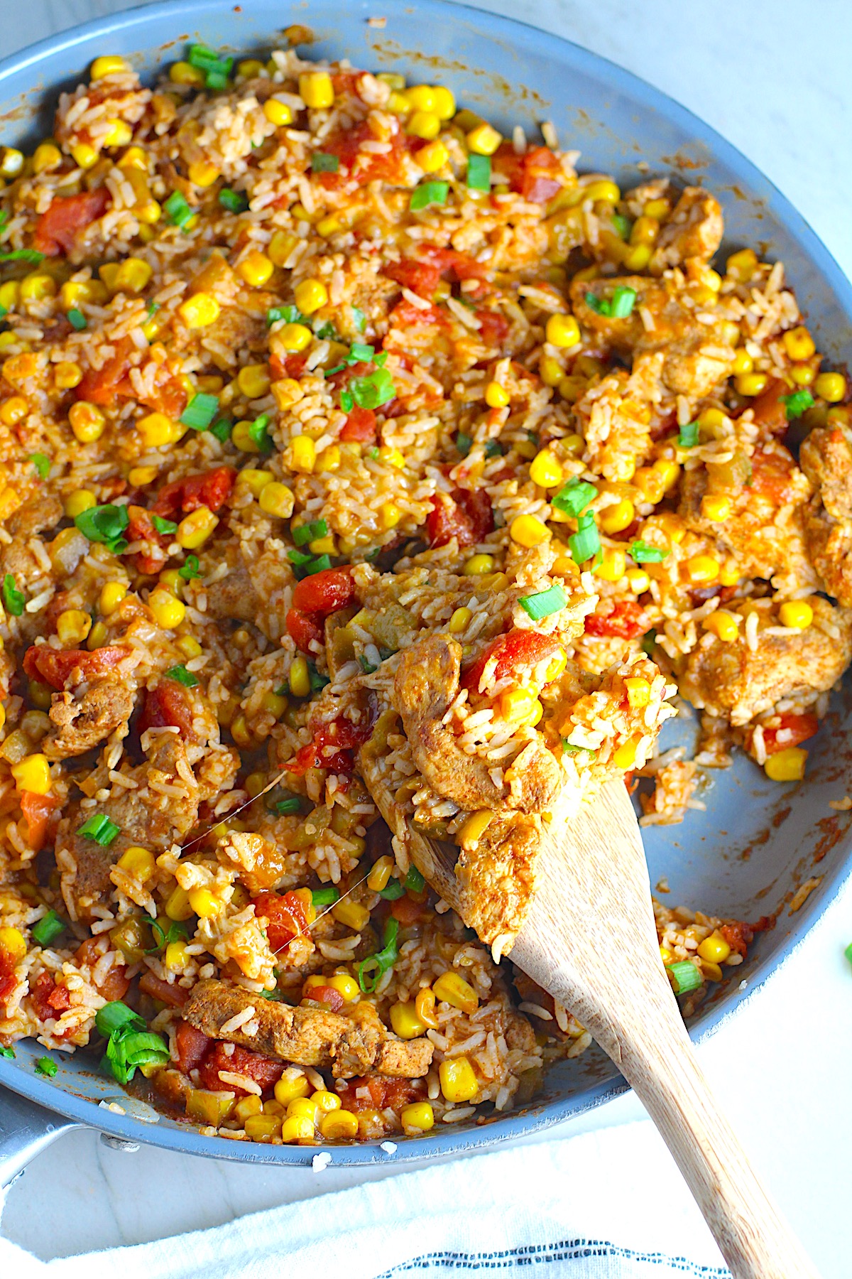 Cheesy Mexican Chicken and Rice Skillet with tomatoes, corn, and scallions. Spatula scooping inside the skillet.