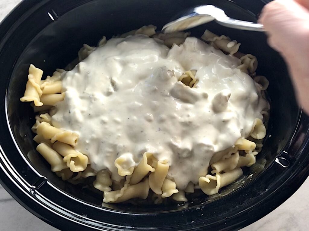 Creamy ingredients added to cooked pasta and chicken in crockpot for Ranch Chicken Crock Pot Pasta recipe. It uses fresh dill, parsley, and scallions is creamy, tangy, and utterly delicious! It's also so easy to make, so it's a great weeknight dinner.