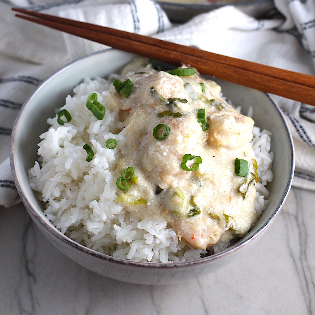 Creamy Chinese Coconut Shrimp Recipe over rice in bowl garnished with scallions and chopsticks on edge of bowl. It's filled with flavor from garlic, ginger, coconut, and more. Done in under 30 minutes, it's perfect for busy nights!