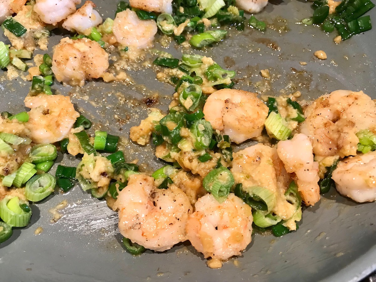 Shrimp, garlic, ginger, and scallions cooking in pan for Creamy Chinese Coconut Shrimp Recipe. It's filled with flavor from garlic, ginger, coconut, and more. Done in under 30 minutes, it's perfect for busy nights!