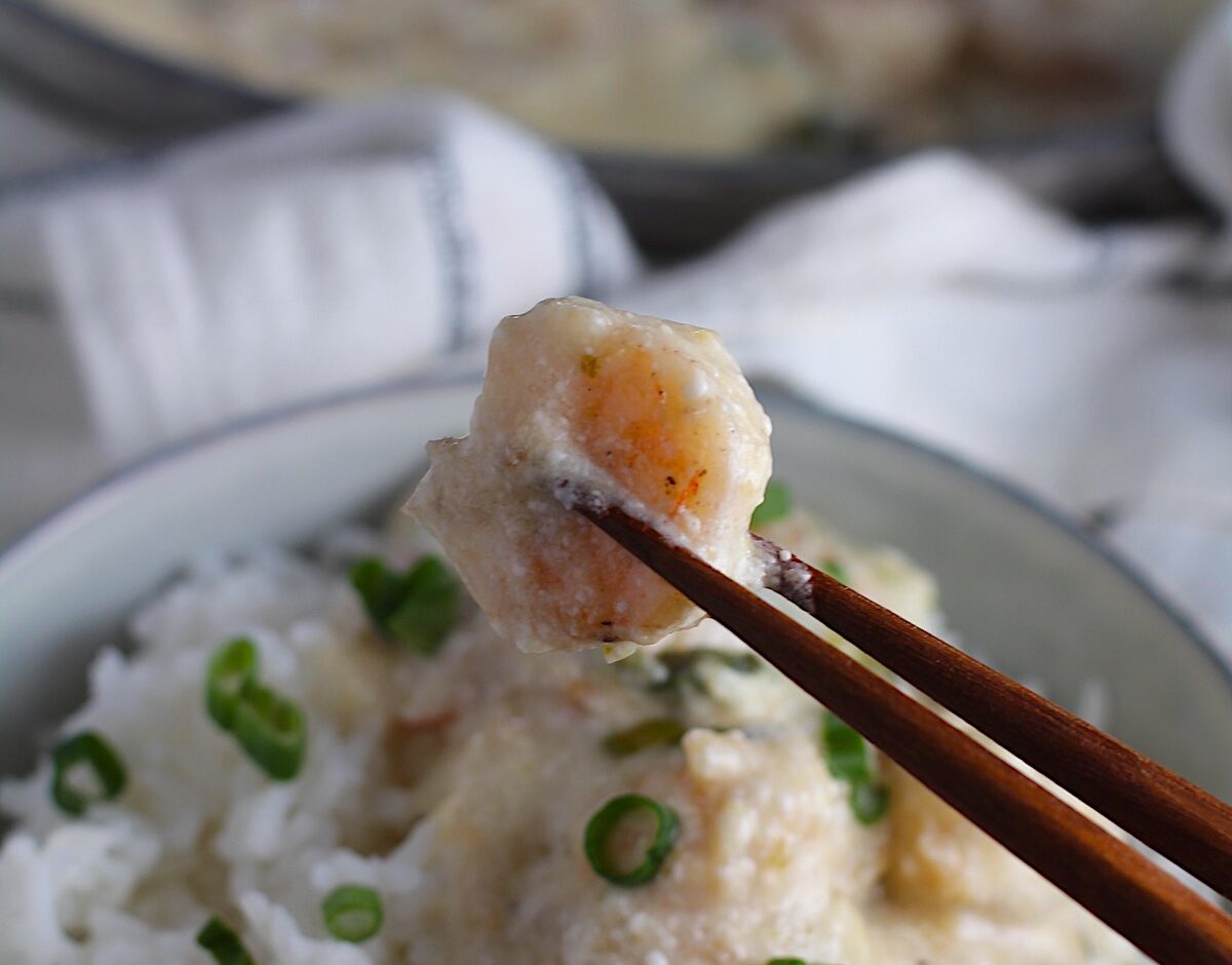 Creamy Chinese Coconut Shrimp Recipe over rice in bowl garnished with scallions and chopsticks on edge of bowl. It's filled with flavor from garlic, ginger, coconut, and more. Done in under 30 minutes, it's perfect for busy nights!