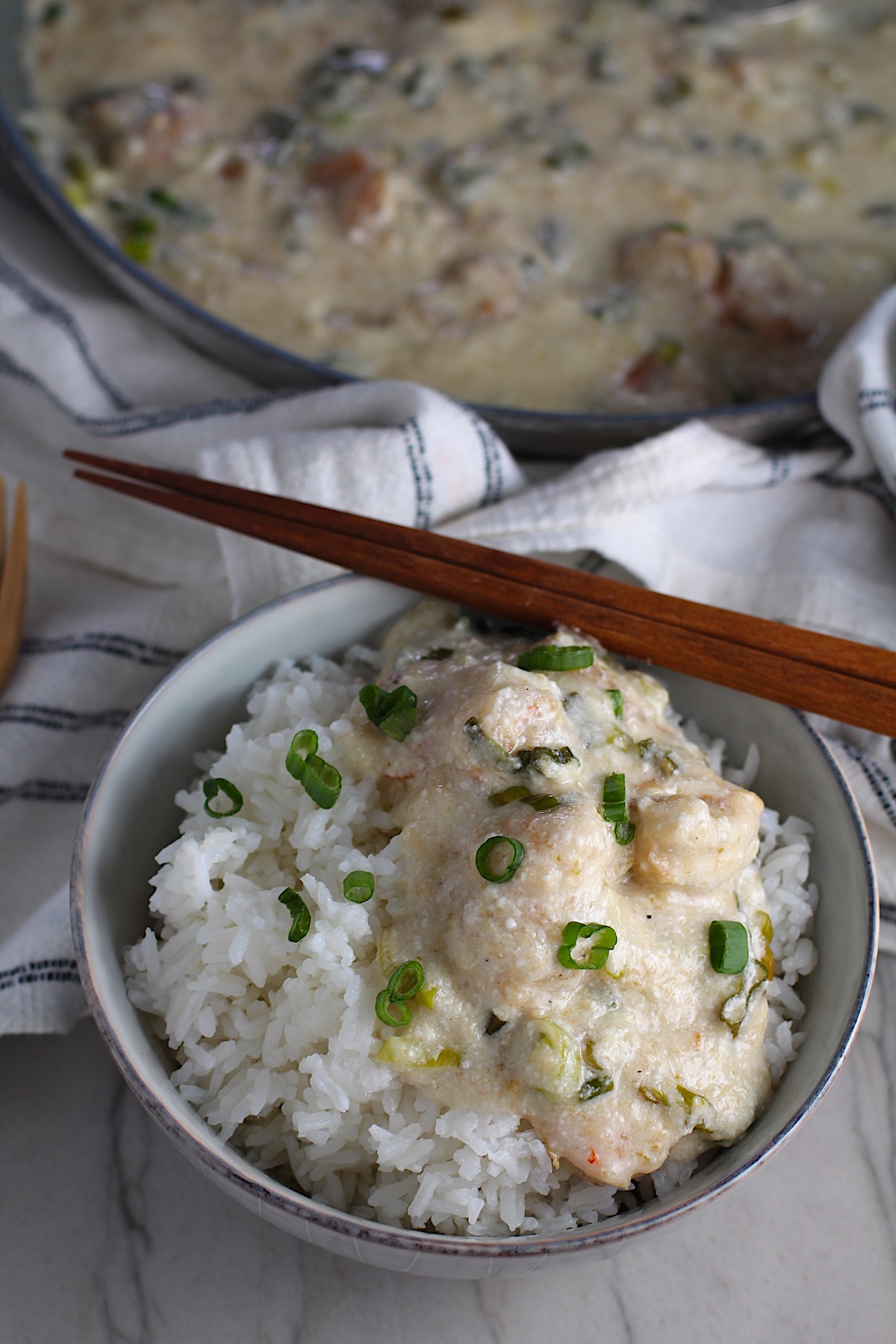 Creamy Chinese Coconut Shrimp Recipe over rice in bowl garnished with scallions and chopsticks on edge of bowl. It's filled with flavor from garlic, ginger, coconut, and more. Done in under 30 minutes, it's perfect for busy nights!