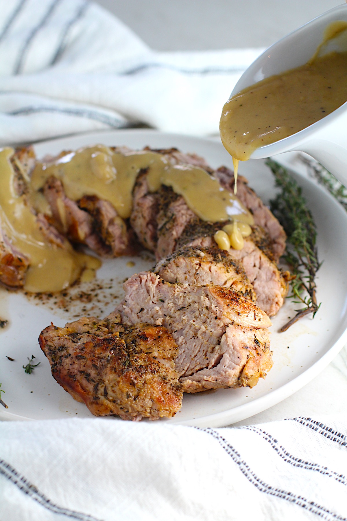 Gravy server pouring thick gravy over sliced roast pork tenderloin. This Roast Pork Gravy Recipe is thick, creamy, and full of flavor.