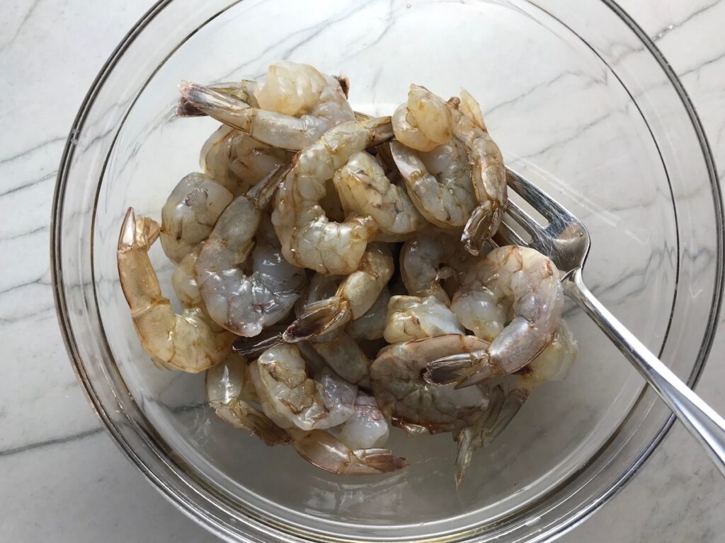 Raw shrimp in a bowl with seasonings for Shrimp Mei Fun Recipe, Singapore Noodles. It's an easy stir fry to make at home and tastes so much better than take out! With carrots, bean sprouts, curry powder, sesame oil, and more it's is a 30 minute weeknight dinner.
