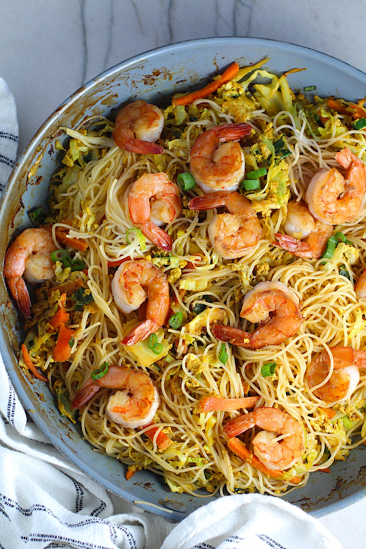 Shrimp Mei Fun Recipe, Singapore Noodles, in a pan on counter. It's an easy stir fry to make at home and tastes so much better than take out! With carrots, bean sprouts, curry powder, sesame oil, and more it's is a 30 minute weeknight dinner.
