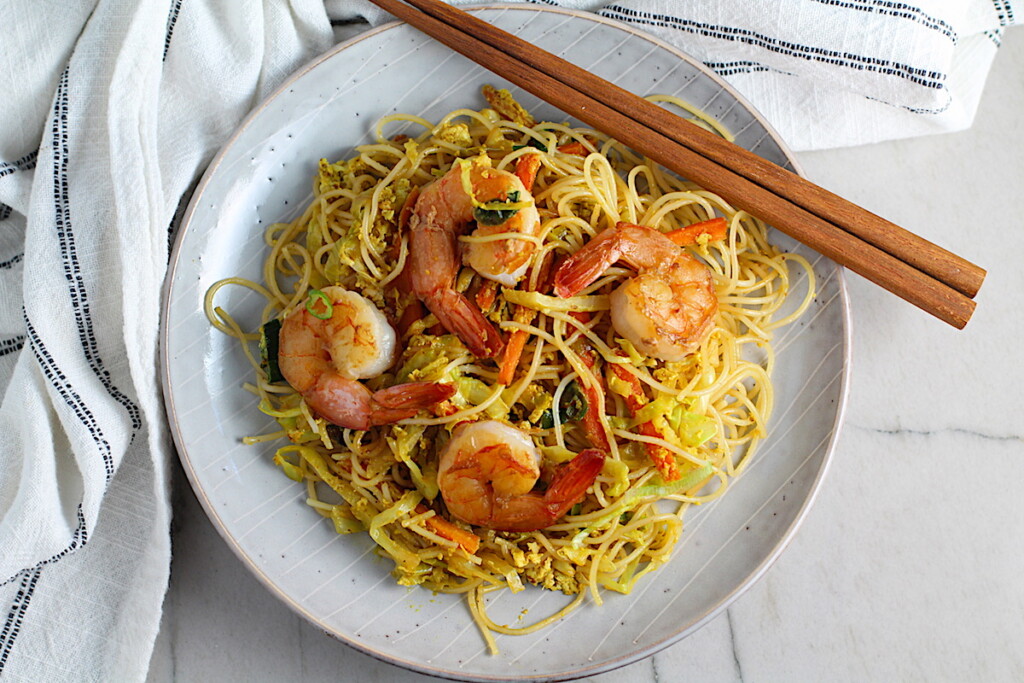 Shrimp Mei Fun Recipe, Singapore Noodles, on a plate with brown wood chop sticks on counter with napkin. It's an easy stir fry to make at home and tastes so much better than take out! With carrots, bean sprouts, curry powder, sesame oil, and more it's is a 30 minute weeknight dinner.