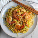 Shrimp Mei Fun Recipe, Singapore Noodles, on a plate with brown wood chop sticks on counter with napkin. It's an easy stir fry to make at home and tastes so much better than take out! With carrots, bean sprouts, curry powder, sesame oil, and more it's is a 30 minute weeknight dinner.