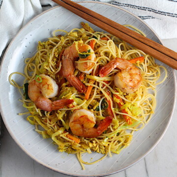 Shrimp Mei Fun Recipe, Singapore Noodles, on a plate with brown wood chop sticks on counter with napkin. It's an easy stir fry to make at home and tastes so much better than take out! With carrots, bean sprouts, curry powder, sesame oil, and more it's is a 30 minute weeknight dinner.