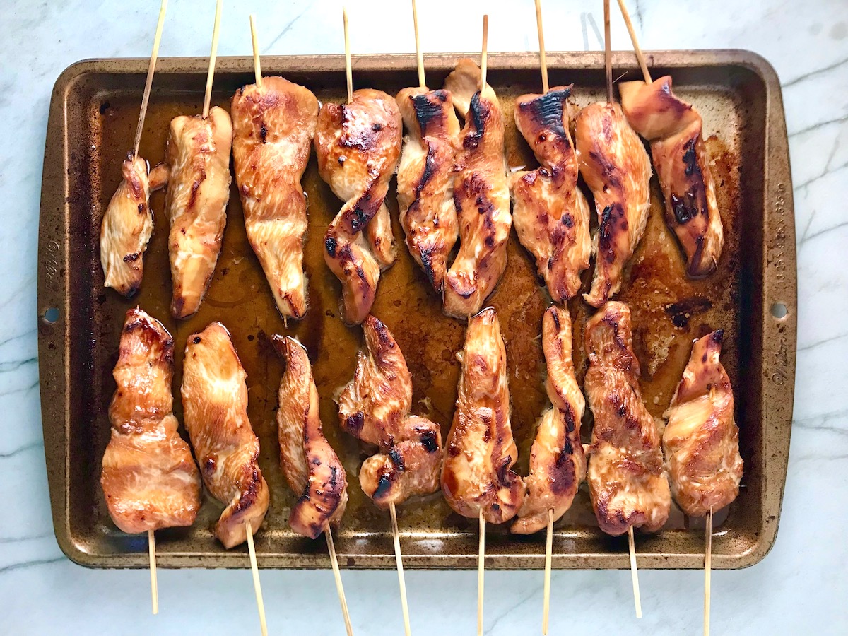 Cooked chicken on skewers on a sheet pan for Chinese Chicken on a Stick Recipe.