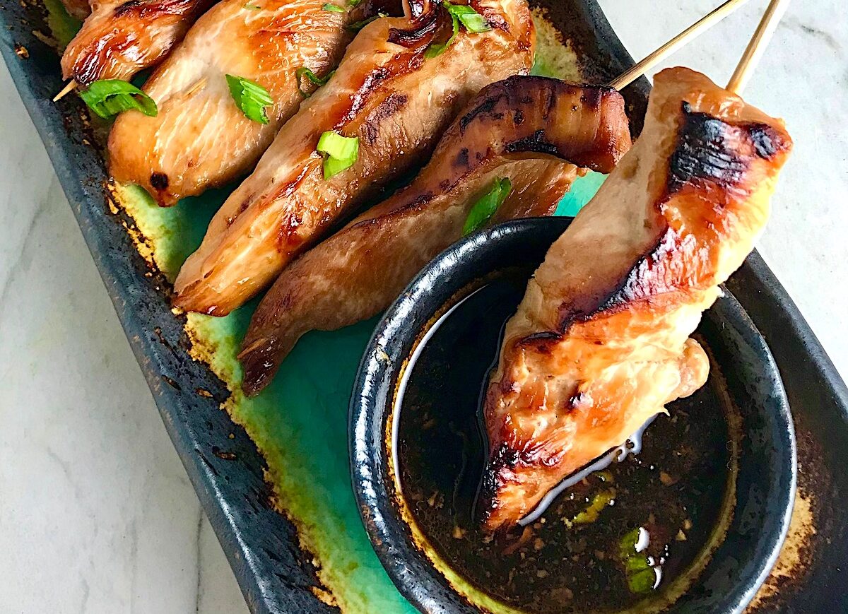 Chinese Chicken on a Stick Recipe on a rectangle platter with small bowl of dipping sauce and pan in background.