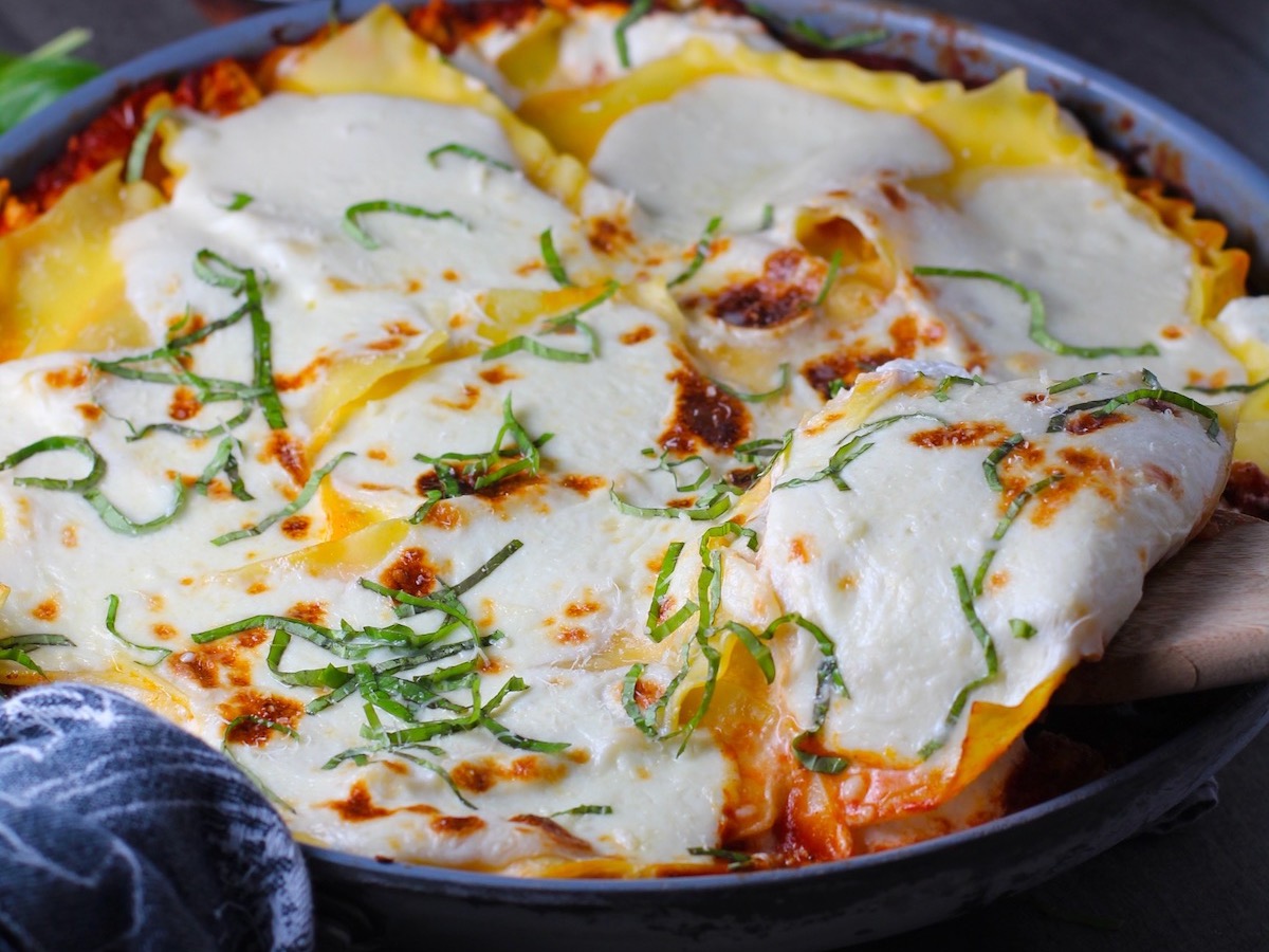 Angle shot of No-Bake Lasagna in skillet with spatula scooping a piece out. It cooks in a skillet or frying pan on the stovetop to save time!