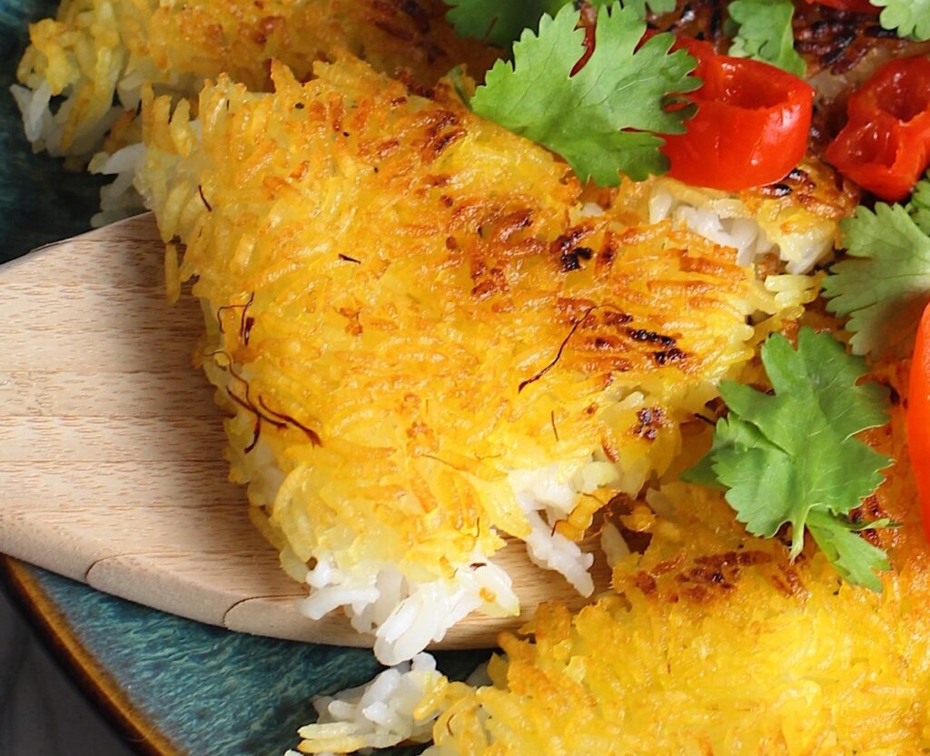 Saffron Butter Crispy Rice on a plate with cilantro and peppadew peppers on top. Spatula scooping up a triangle piece. Saffron brings a floral note and beautiful yellow-orange color. Added to the butter is what gives this crispy rice the buttery, crispy bottom.