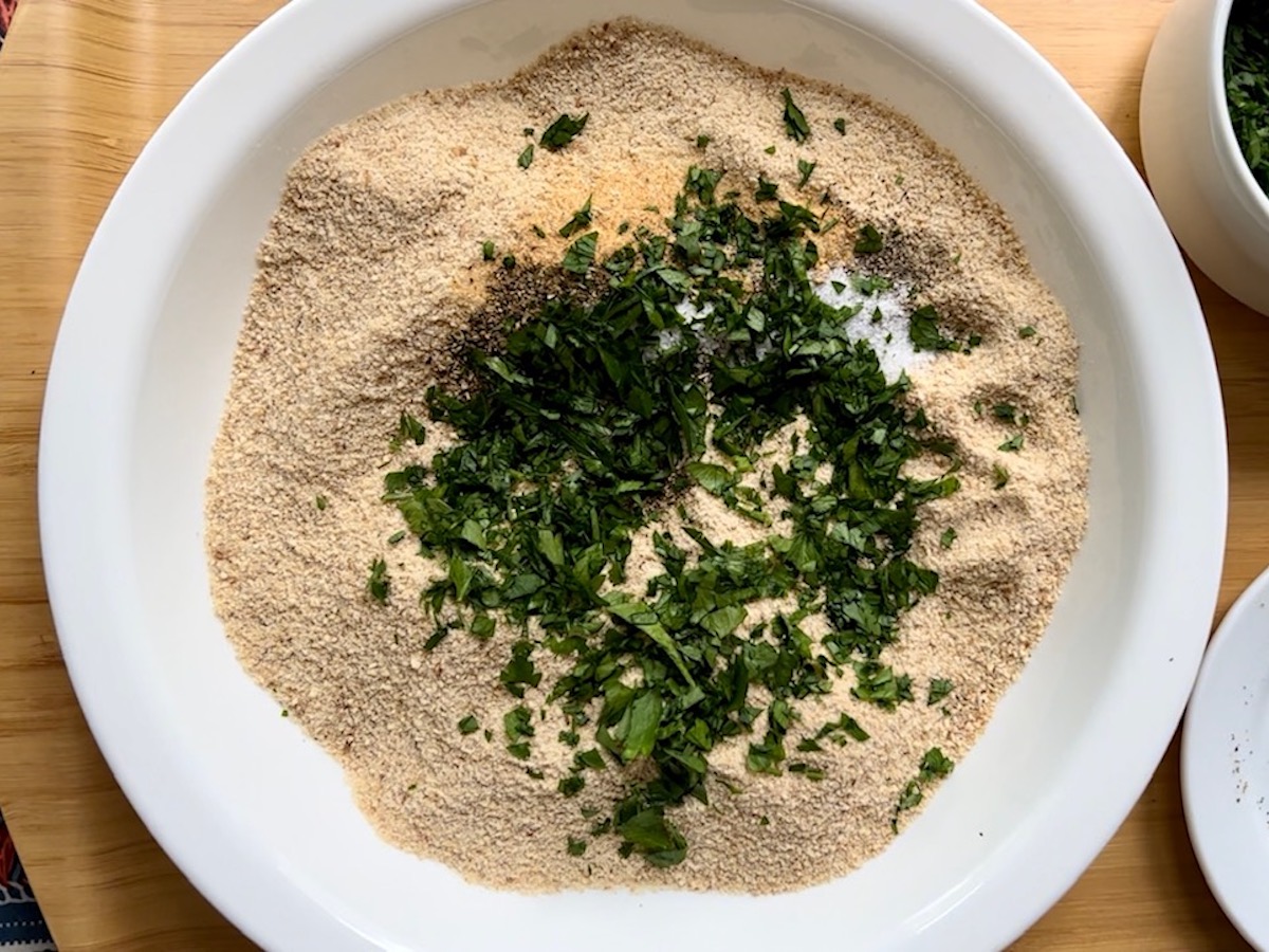 Breadcrumbs, salt, pepper, garlic powder, and fresh parsley in large bowl for Italian Chicken Cutlets.