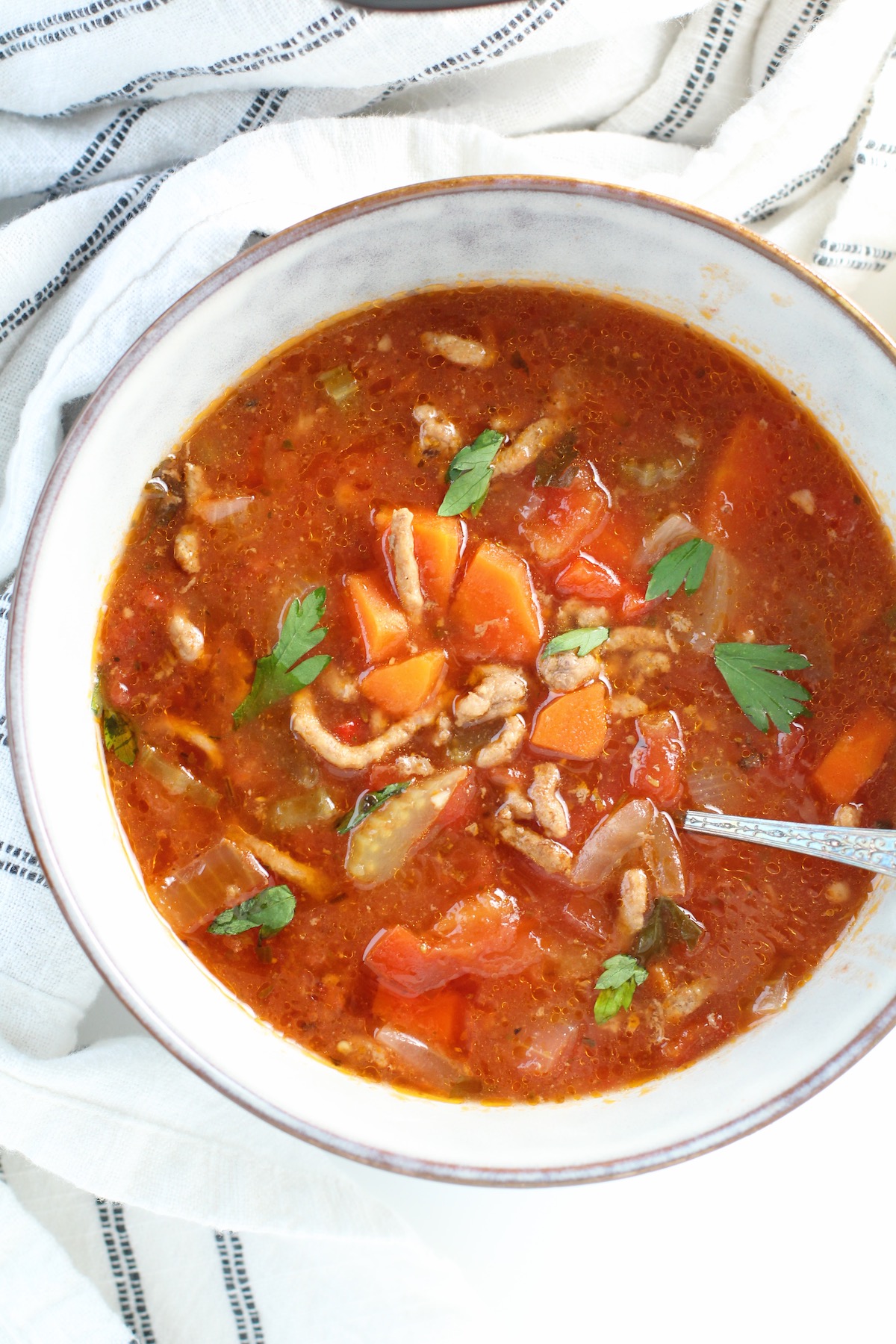 Ground Beef Vegetable Soup Recipe in a bowl with spoon on counter with blue and white towel around. It's a perfect fall meal that's comforting, hearty, and delicious with loads of veggies! Make it in the slow cooker or on the stove.