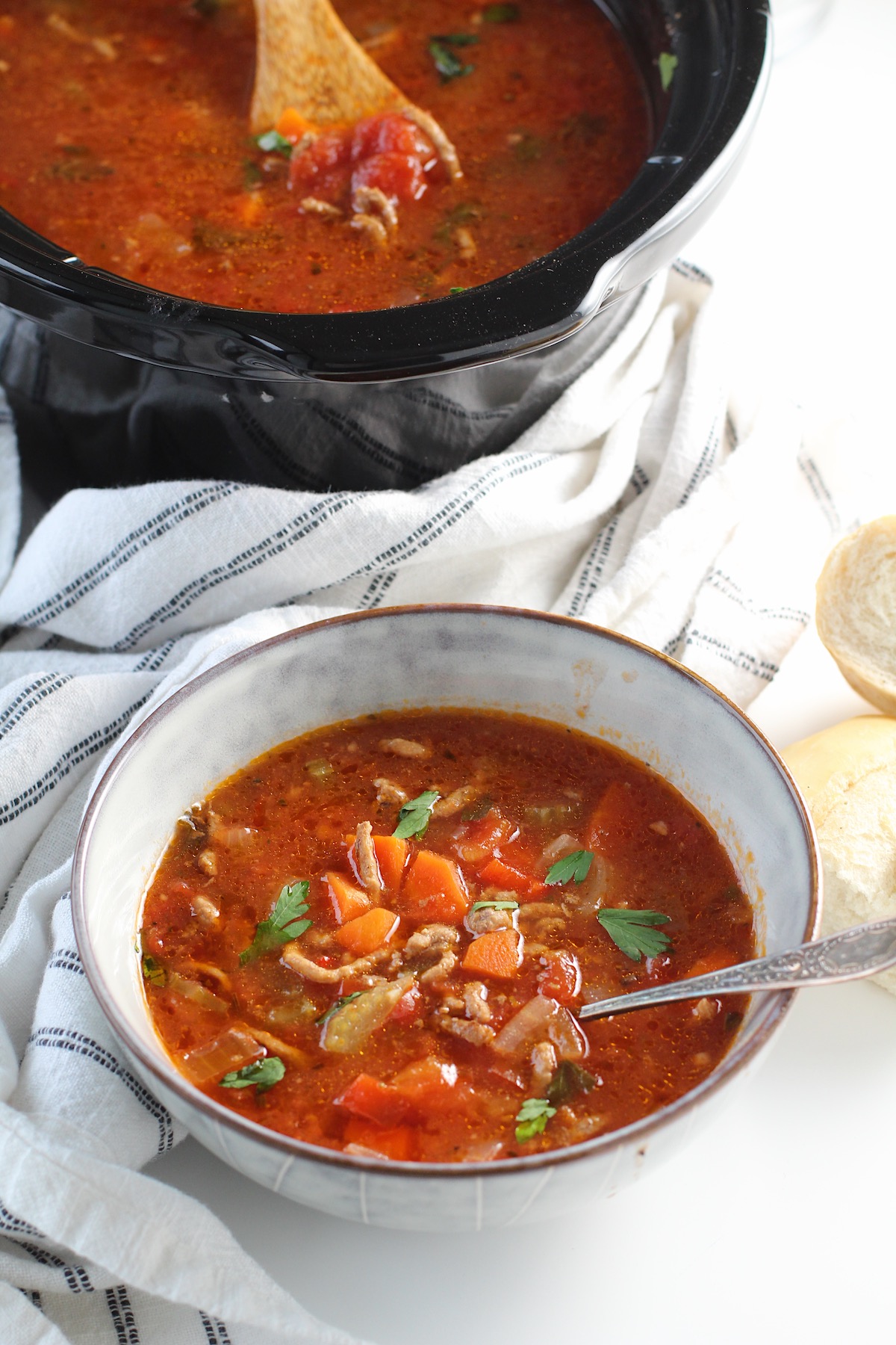 Ground Beef Vegetable Soup Recipe in a bowl with spoon on counter with blue and white towel around and slow cooker in background.  It's a perfect fall meal that's comforting, hearty, and delicious with loads of veggies!  Make it in the slow cooker or on the stove.