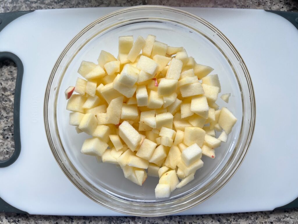 Peeled and diced apples in a clear bowl on cutting board for Pork Normandy recipe.
