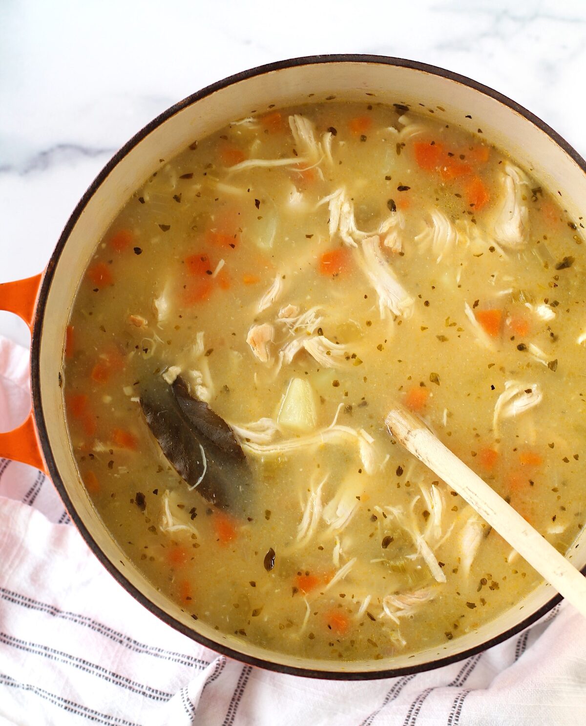 Creamy Chicken Potato Soup Recipe with carrots and celery in a dutch oven with a wood spoon on counter with towel. It's comforting, hearty, and delicious. It's a great dinner for busy families!