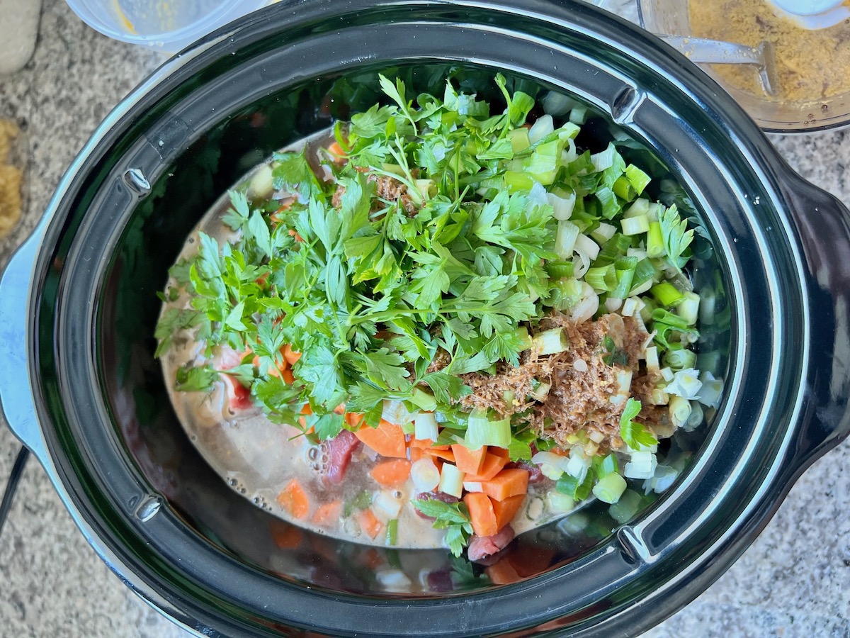 Beef broth, raw carrots, celery, scallions, and cilantro added to beef in slow cooker for Korean Beef Stew.