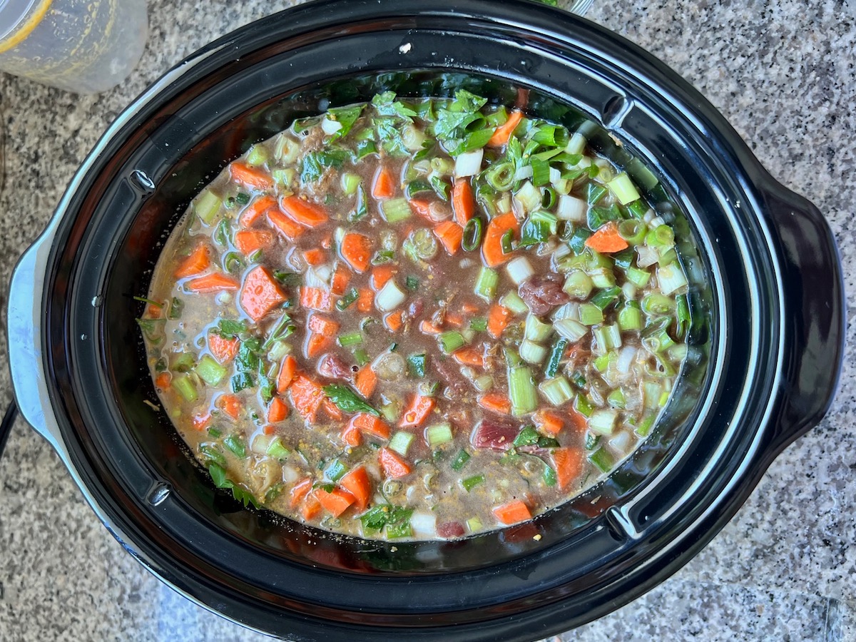 All ingredients mixed, including beef broth, raw carrots, celery, scallions, and cilantro added to beef in slow cooker for Korean Beef Stew.