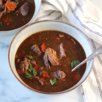 Two bowls of Korean Beef Stew, one with a spoon, on counter with blue and white striped towel. Korean Beef Stew is sweet, salty, tangy, and oh-so flavorful!