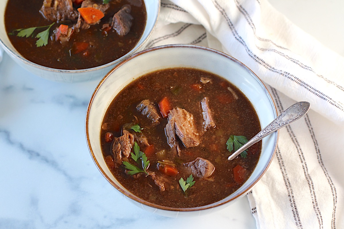 Two bowls of Korean Beef Stew, one with a spoon, on counter with blue and white striped towel. Korean Beef Stew is sweet, salty, tangy, and oh-so flavorful!