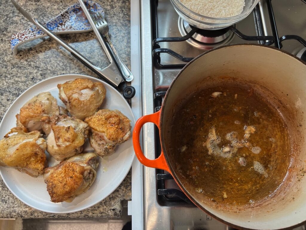 Seared chicken thighs transferred from the pot to a plate with fat left behind in the pot for Roasted chicken rice.