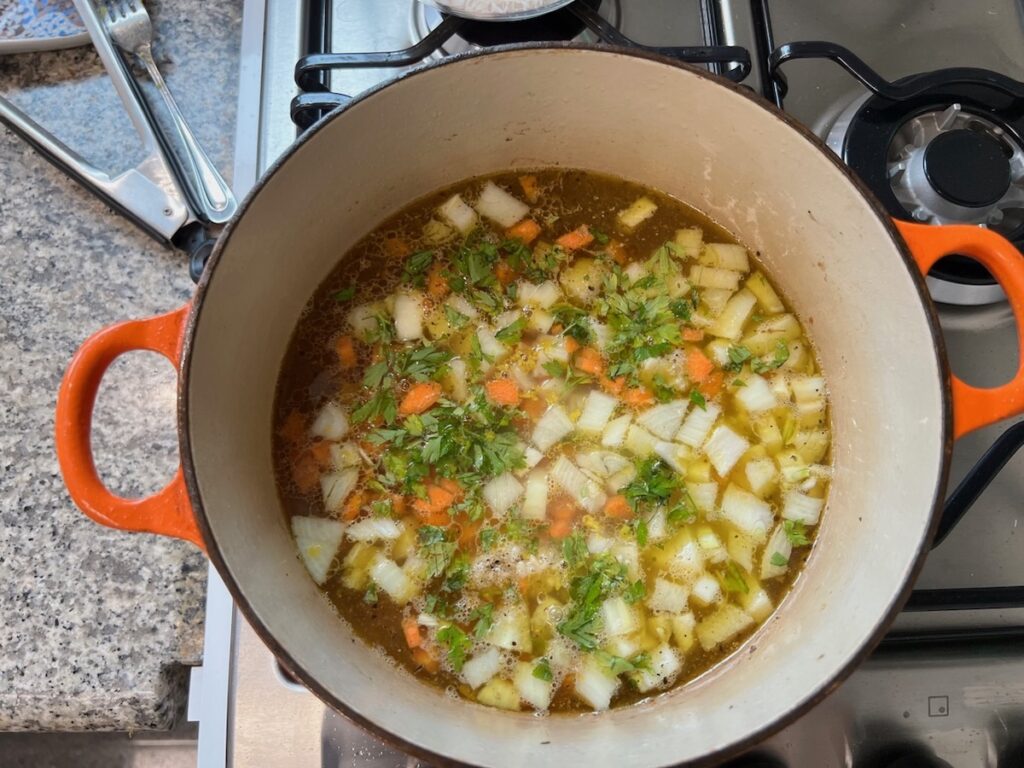 Carrots, onions, parsley, and broth cooking in a pot for Roasted chicken rice.