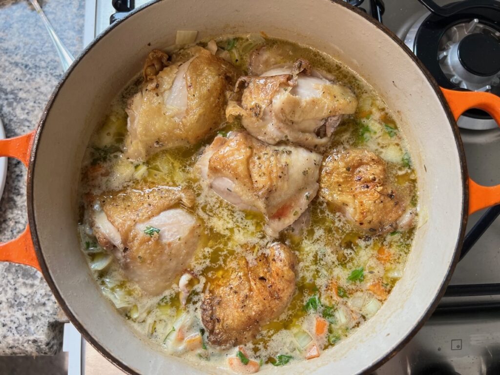 Chicken thighs added to rice, carrots, onions, parsley, and broth cooking in a pot for Roasted chicken rice.