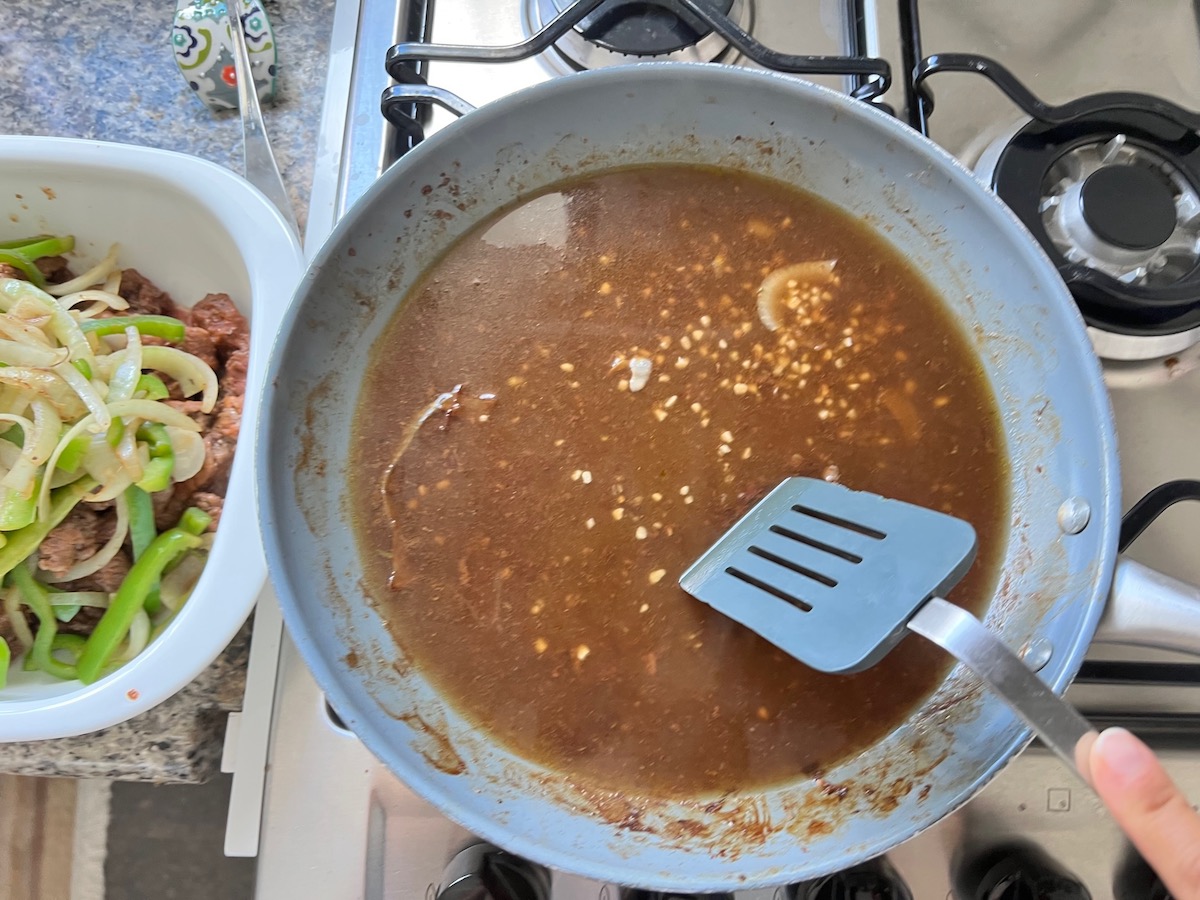 Onions and green peppers transferred to casserole dish and spatula scraping up the skillet with broth in it for Philly Cheesesteak casserole recipe with Steak.