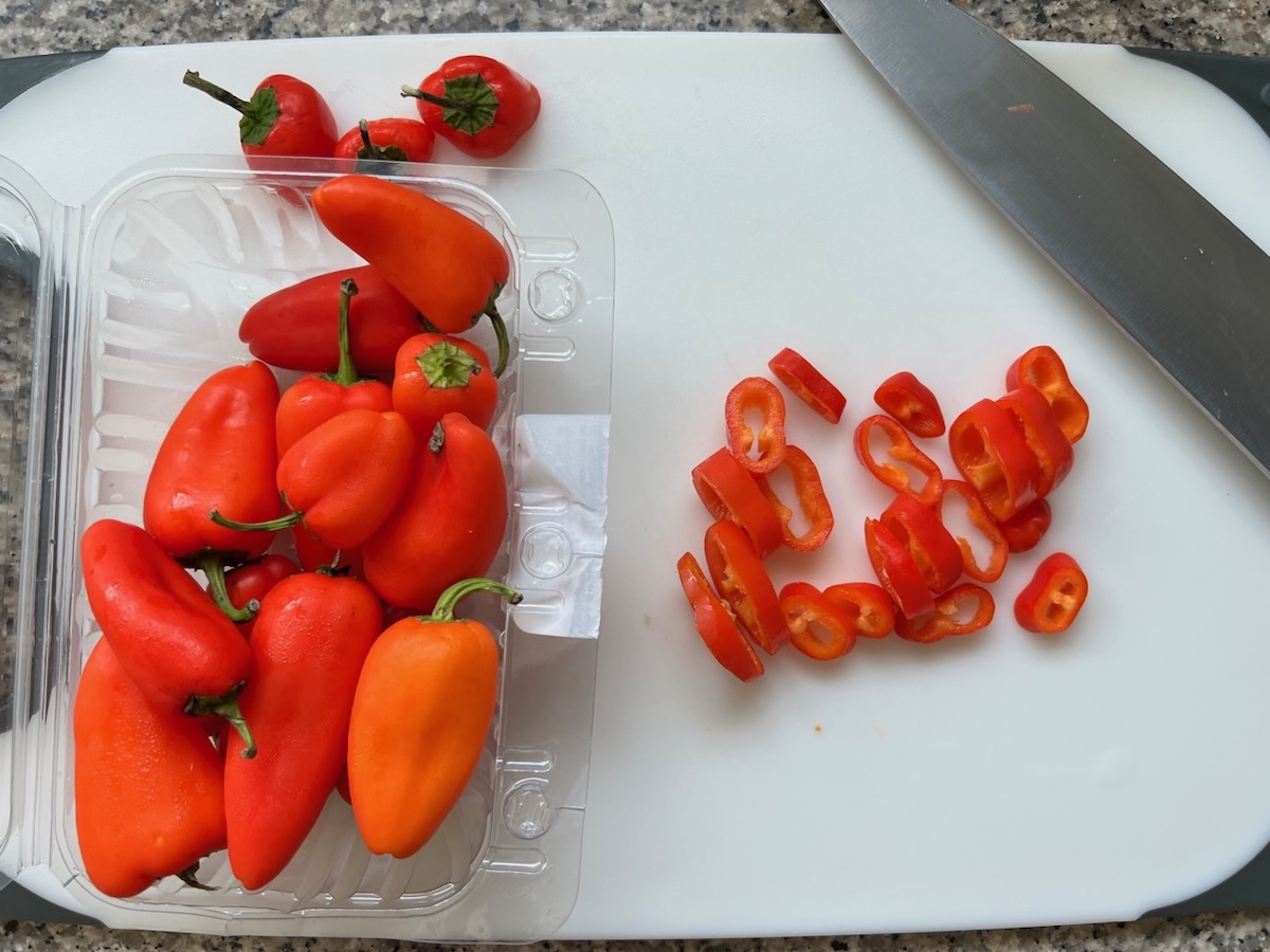 Mini sweet red peppers in the package next to some the have been sliced on the cutting board for this Thai Basil Pork Recipe.