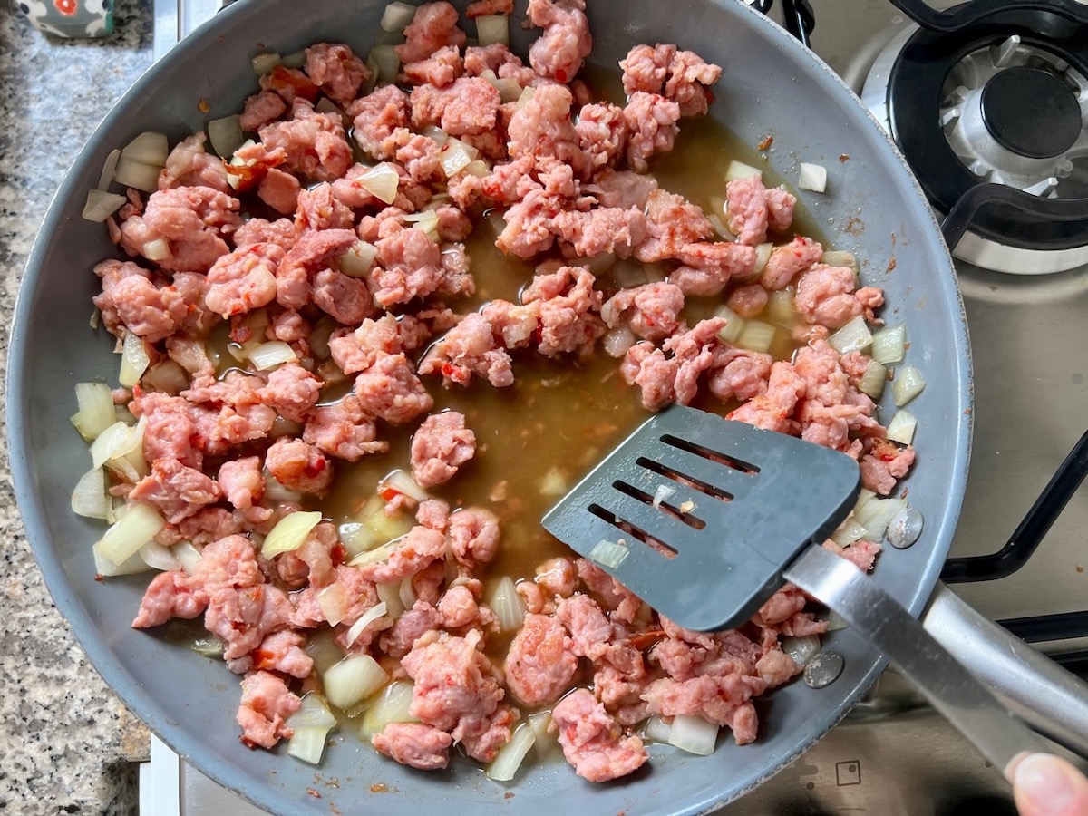 Spatula scraping bottom of pan with broth, ground pork and onions cooking in a skillet for Thai Basil Pork recipe.