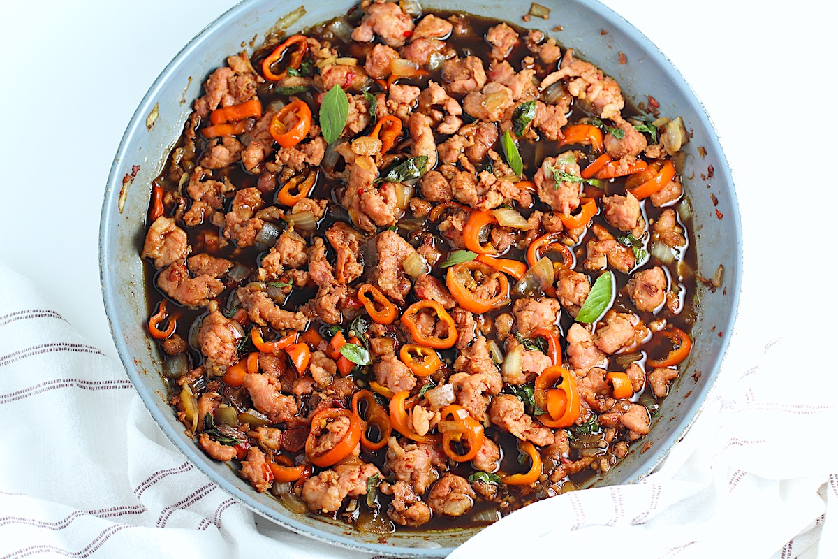 Thai Basil Pork Recipe with mini red pepper slices in a skillet on the counter with a towel wrapped around the handle.