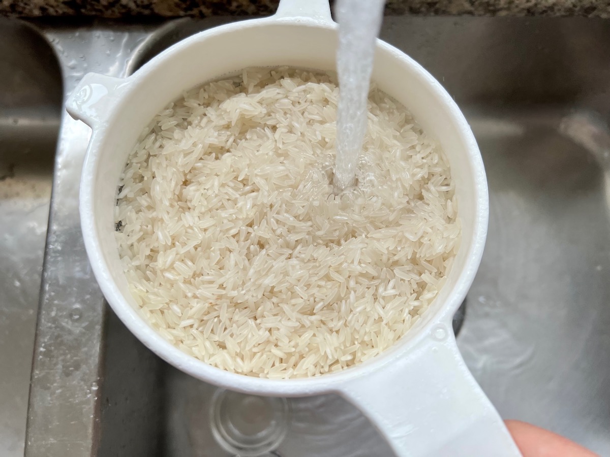Uncooked rice in a strainer being rinsed under the sink water for Salsa Chicken Casserole Recipe.