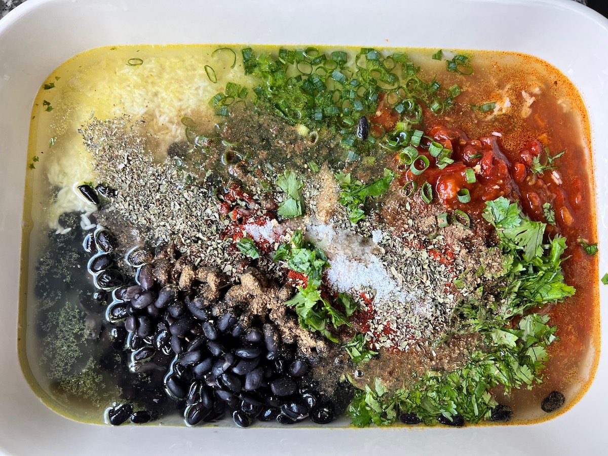 Black beans, seasonings, cilantro, salsa, rice, and broth in casserole dish before mixing it for Salsa Chicken Casserole Recipe.