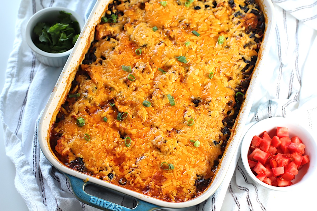 Salsa Chicken Casserole Recipe with cheese melted on top and scallions sprinkled over. A bowl of tomatoes is in the lower right and cilantro in the upper left.