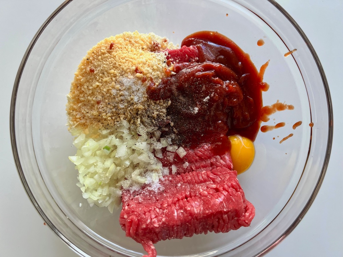 Raw ground beef, diced onion, ketchup, egg, and parmesan in bowl before being mixed together for Meatloaf Casserole Recipe.