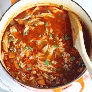 Spanish Chicken Soup in a pot with a wooden spoon on table.