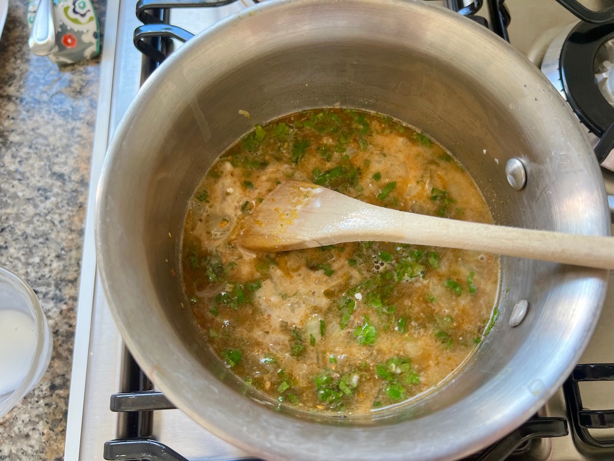 All ingredients for the enchilada sauce in a pot with wood spoon for crockpot white chicken enchilada casserole.