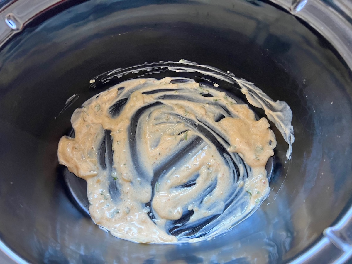 White enchilada sauce added to the bottom of the crockpot before layering in the tortillas and chicken for crockpot white chicken enchilada casserole.