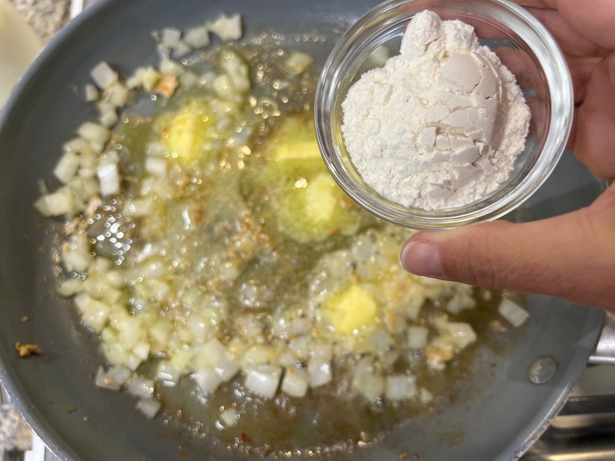 Hand holding flour over a frying pan with butter and onions for Chicken Divan Curry Casserole Recipe.