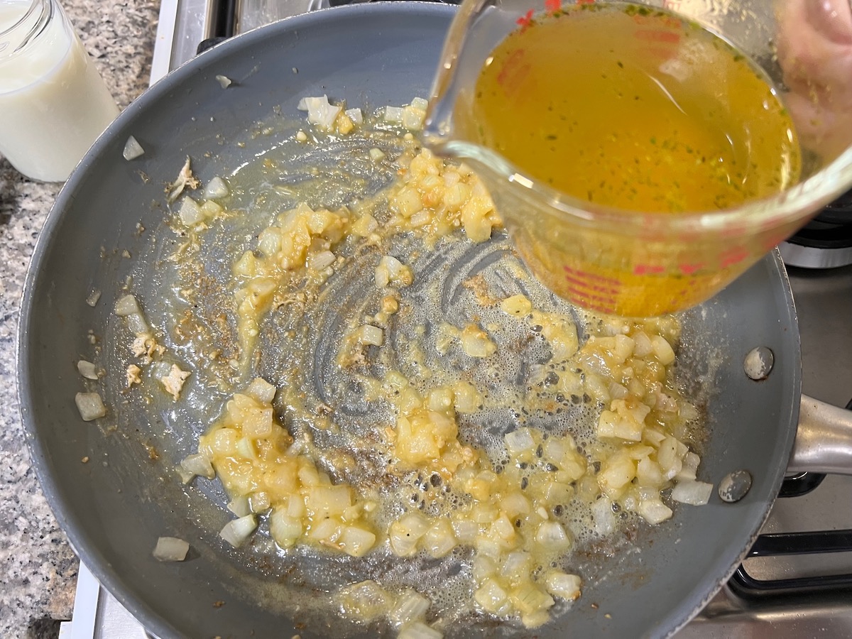 Pouring broth from a measuring cup into the onions, butter, flour mixture in a frying pan for Chicken Divan Curry Casserole Recipe.
