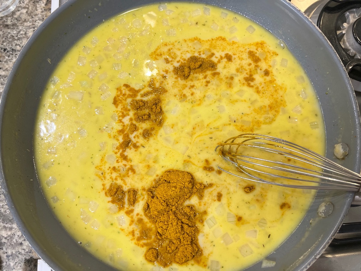Spatula whisking curry powder into the sauce in a frying pan for Chicken Divan Curry Casserole Recipe.