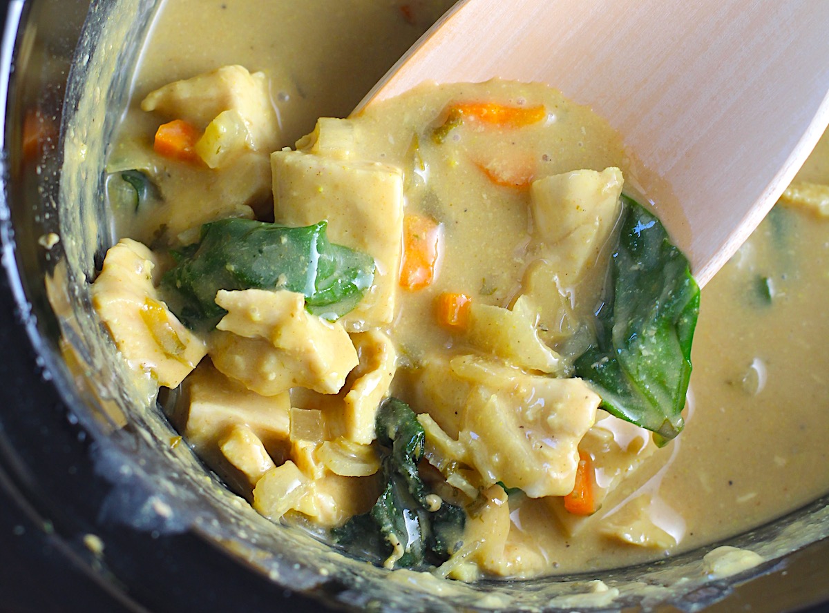 Crockpot Thai Chicken Curry over rice in a slow cooker with wooden spoon.