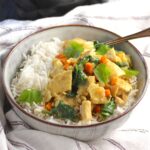 Crockpot Thai Chicken Curry over rice in a bowl with fork and slow cooker in background.