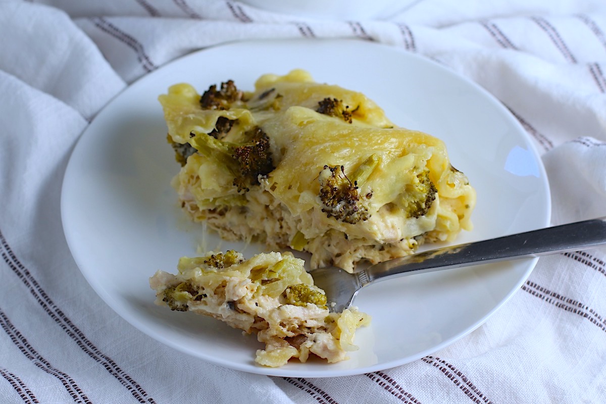 Piece of Broccoli and Chicken Lasagna on plate with fork laying down on the plate holding a bite.