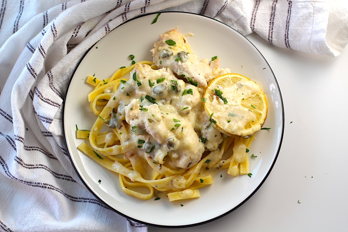 Creamy Chicken Piccata Casserole Recipe served on a plate over pasta with the casserole dish in the background.