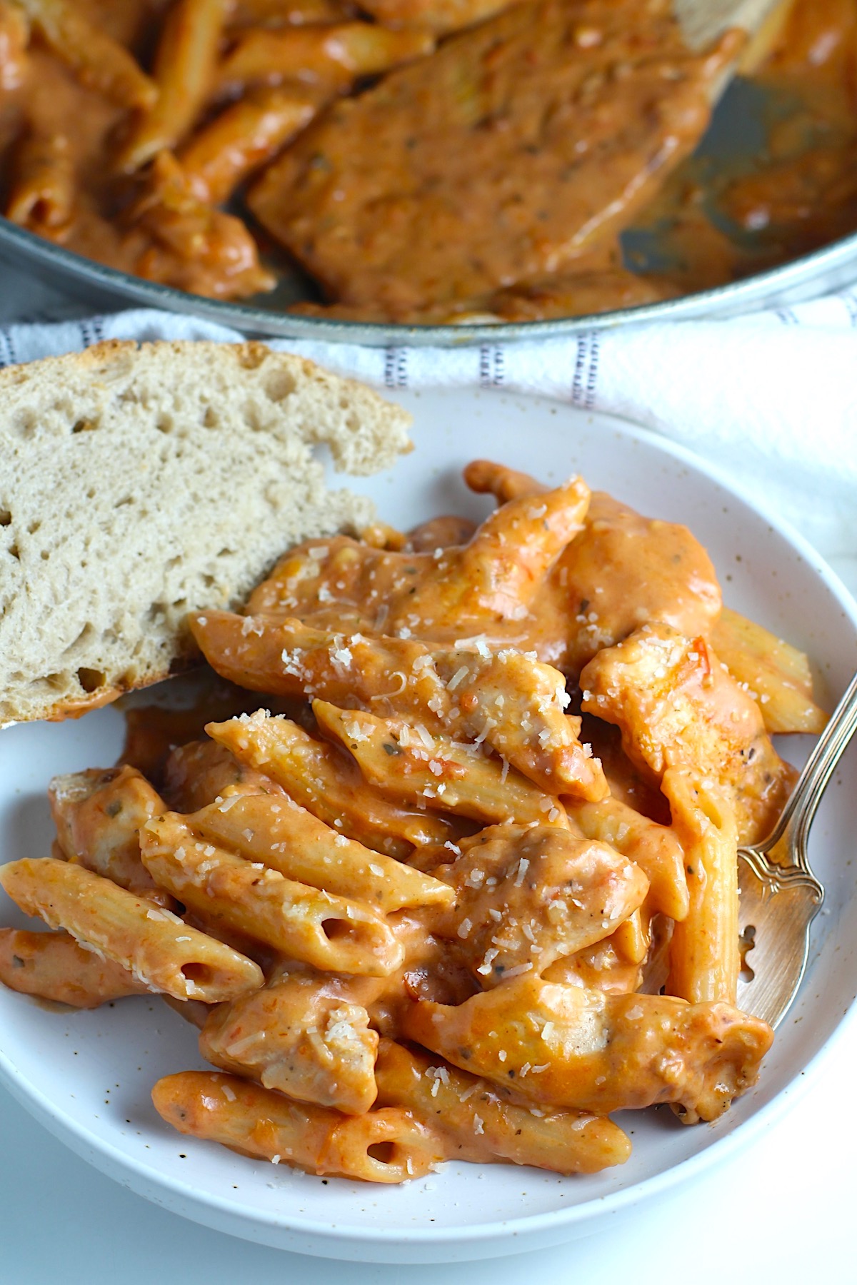 Chicken and Vodka Pasta on a plate with fork and a slice of crusty bread and pan in background..