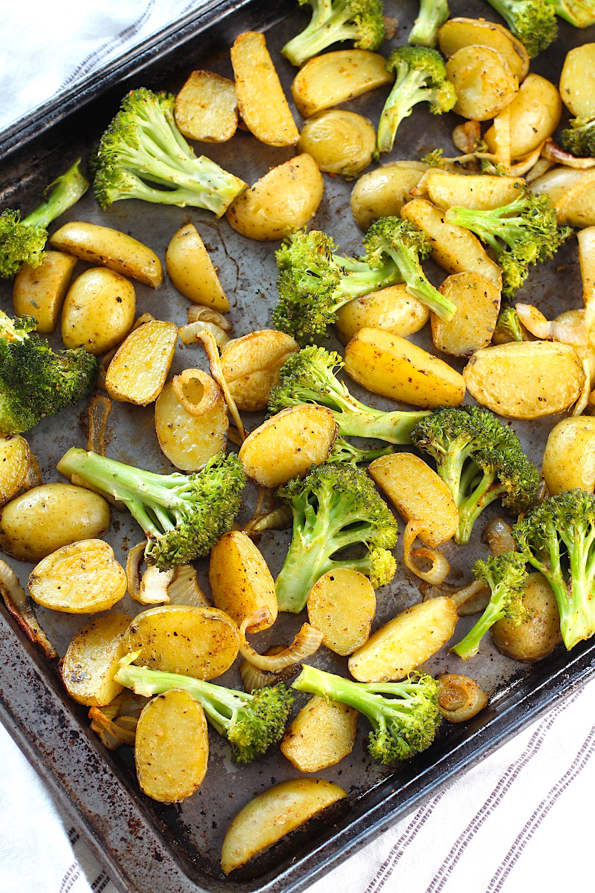Roasting Potatoes and Broccoli with onions on a sheet pan. The potatoes are cut, golden brown, and crispy. The broccoli is toasty and tender.