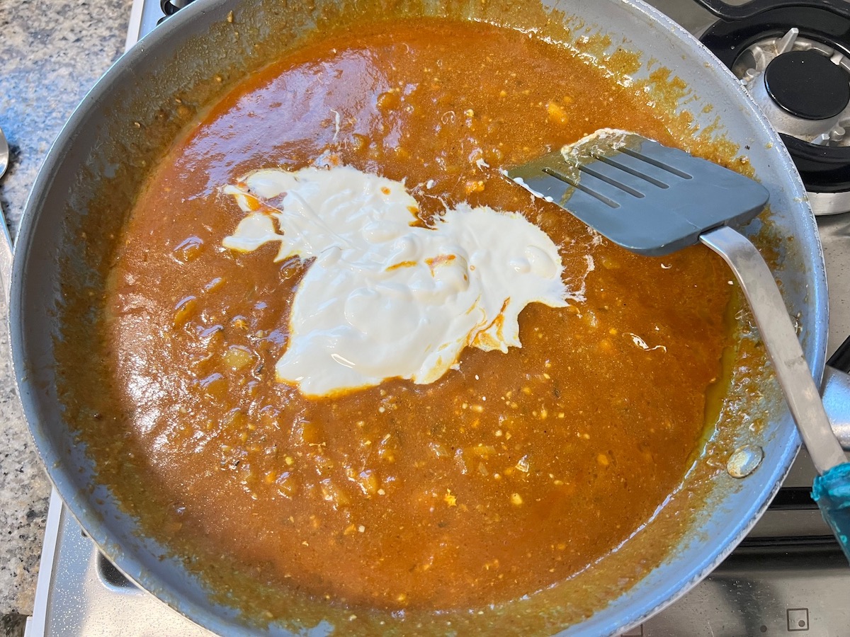 Heavy cream added to the tomato mixture in a skillet for butter chicken pasta.